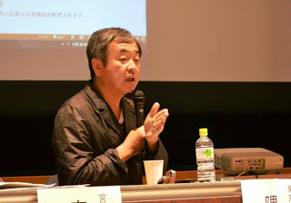 スクリーンの前に座りマイクを持った隈氏が話をしている様子をアップで撮影した写真