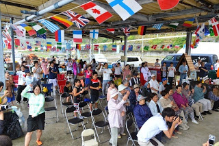 屋根付きの会場に多くの観客が集まり、立って踊る人や座って見ている人が一緒に盛り上がっている様子の写真