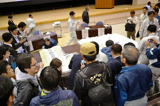 沢山の人たちが大きな図面の様な資料が置かれたテーブルを囲み熱心に見ている様子を写した写真