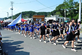 運動部のユニフォーム姿の学生たちが整然と行進し、大きな青白の旗を掲げている写真