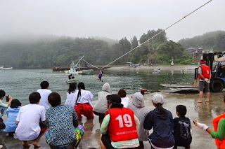 岸から多くの人が見守るなか、海上をロープで滑空する参加者が海に近づいている様子の写真