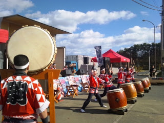 赤の法被を着た和太鼓の演奏者たちが大きな太鼓を力強く叩いているステージ演奏の写真