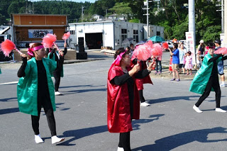 ピンクのポンポンを両手に持ち、お揃いの赤と緑の光沢のある衣装を着た人たちが踊っている写真