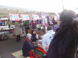 屋台が並ぶ通路の一角に置かれたこたつを囲んだ人たちがお茶を飲みながら談笑している写真