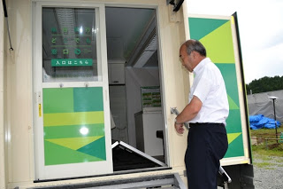 白いシャツの男性が、移動銀行車の入口ドアを開けて中にある床板が折り畳まれている部分を写した写真