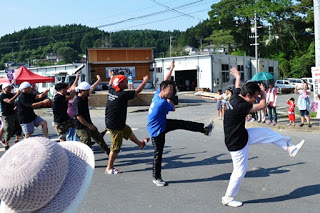 男性のチームが一列に並び、左足を高く上げ、両手を左側に上げてがら踊りのパフォーマンスをしている写真
