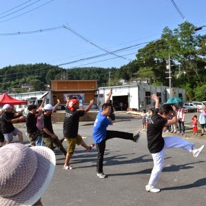 黒いTシャツに身を包んだ男性たちが、片足を大きく上げ、上げた方に向かって両手を伸ばして踊っており、陽気な振り付けで観客を盛り上げている男性グループのトコヤッサイコンテストの写真
