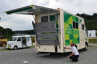 後部に設置された車椅子対応のリフトを、男性が地面にしゃがんで操作している様子を写した写真
