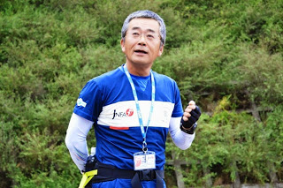 青いスポーツウェアを着た男性が、名札をつけて野外で話をしている様子をアップで撮影した写真