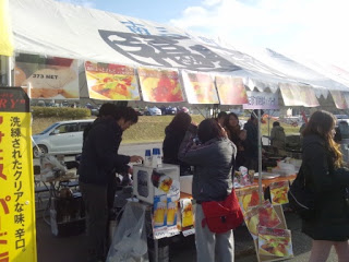 飲食ブースのテントの下で店員が注文を受けて料理を提供し、来場者が出来上がるのを待っている写真