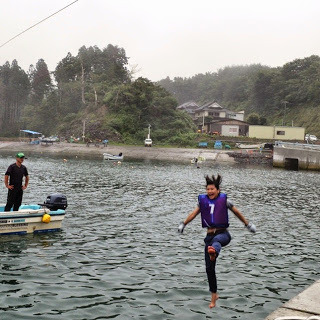 ロープから勢いよく飛び込んだ女性が足を高く上げながら海に落ちる瞬間の写真