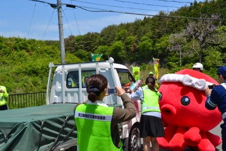オクトパス君の着ぐるみと数人のスタッフが軽トラックに近づき、運転手に啓発物を手渡している交通安全イベントの写真