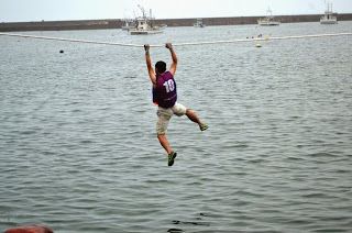 ライフジャケットを着た男性が、海の上に張られたロープを握って渡りながら「海の綱渡り」の種目に参加している様子の写真