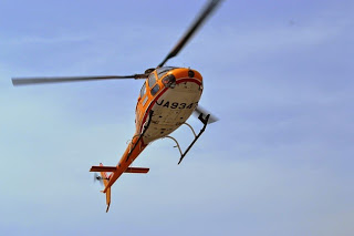 青空の中、オレンジ色のヘリコプターが上昇していく姿を下からとらえた写真