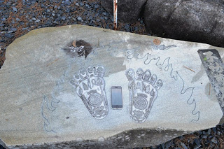 平らな石に炎と大聖不動明王の足跡が刻まれ、足の間にiPhoneが置かれている写真