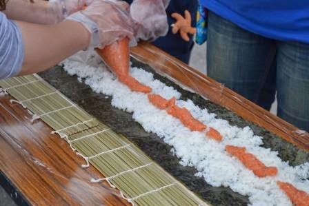 巻きすを広げた長い海苔の上にご飯を広げて、伊達のぎんを載せて巻き寿司を作っている様子の写真