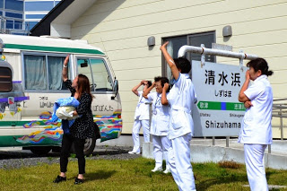 「清水浜」の看板のある建物前で、白衣の看護師たちがヘリコプターに向かって手を振って見送っている写真