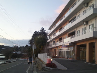 道路沿いに建つ白い4階建ての建物『特別養護老人ホーム いこいの海 あらと』の外観を写した写真