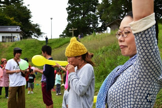 女性が手を高く上げて合図を出しており、他の参加者たちは風船を膨らませながら笑顔で楽しんでいる写真