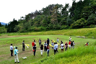 草に囲まれた広場で多くの人が輪になって集まり、バルーンを持ちながらイベントに参加している写真