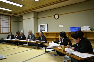 和室の長机にスーツ姿の男性たちが座り、真剣な表情で資料を見ながら話しをしている様子の写真