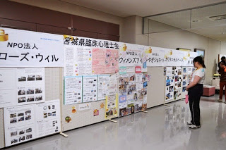 廊下の壁にNPOや団体の活動内容を紹介する写真や資料が多数掲示され、それを来場者が熱心に見ている写真