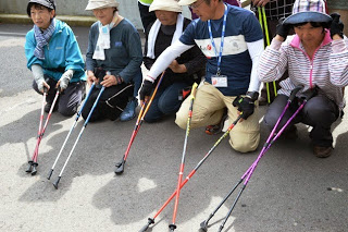 複数の参加者が地面にしゃがみ、色とりどりのトレッキングポールの先をそろえて並べている様子が写っている写真