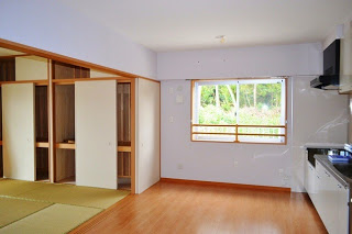 広いリビングルームの左側に畳の部屋と収納スペース、右側にシステムキッチン、奥にある大きな窓から緑の景色が見える様子が写っている写真