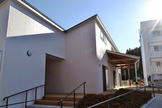 日差しの強い晴天の下、スロープや手すりが設けられている白い外壁の平屋建ての建物外観の写真