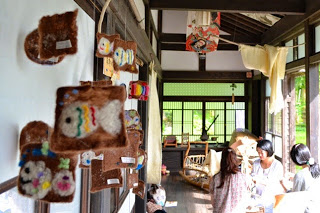 広い縁側の奥で数人の女性が座っており、縁側と室内を隔てた障子沿いにフェルトで作られた魚などの作品が飾られている写真