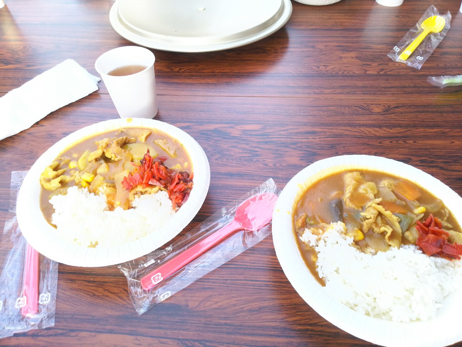 テーブルの上に丸皿に盛られたカレーライスが二つ並んでおり、福神漬けとプラスチック製の箸が添えられている写真