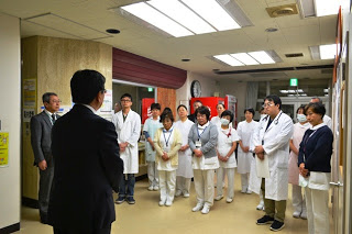 スーツ姿の佐藤町長が医師や看護師など十数名に向かって病院内で話しており、皆が静かに聞いている写真