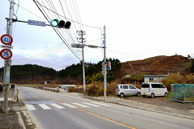 山が削られて造成工事が行われている様子が背景に見える様子を、横断歩道や信号機が取り付けられた道路沿いから撮影した写真