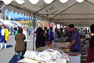 沢山のお客さんが並ぶテントの下で、手作りの食品などを販売する地域の人たちが忙しく対応している写真