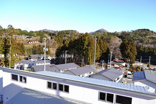 公営住宅の屋根越しに周囲の山や木々、小さな住宅地が広がっている自然に囲まれた集落の写真