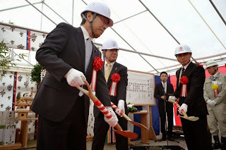 左胸の胸章リボンをつけた白いヘルメットとスーツ姿の男性3人が、儀式用のスコップを持ち地面に砂をすくう動作をしている地鎮祭の写真