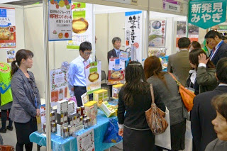 商品が並ぶブースに来場者が集まり、出展者が説明をしている様子を写した地域物産の展示の写真