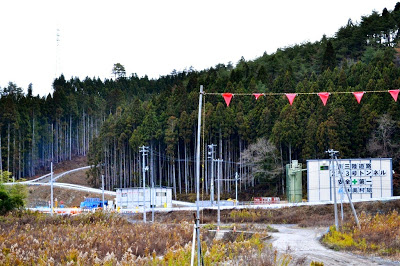 トンネル工事現場で、仮設の建物と重機が設置されている山間部の開発中の写真