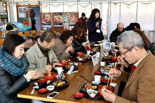 長机を2つくっつけて対面に男女が並んで座り食事を楽しんでいる写真