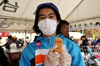 水色のジャンパーとマスク姿の少年が、モアイ像の形をしたモアイ焼きを手に持って見せている写真