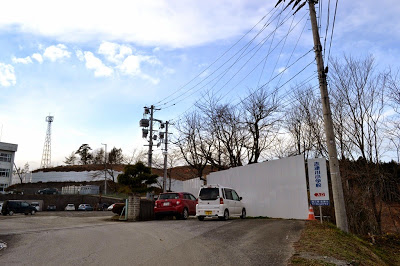 校舎が建っている右側に設置された白い仮囲いの奥で造成工事が進められている様子の写真