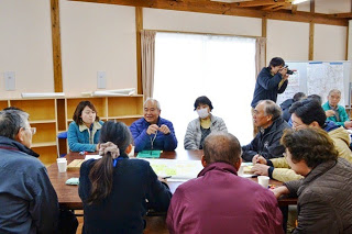 会議室のような場所で円卓を囲んで参加した住民たちが真剣に話し合いをしている地域会合の写真