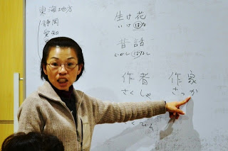 女性講師がホワイトボードに書かれた「作家」の文字を指差しながら発音や意味を説明している様子をアップで撮影した写真