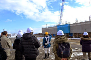 ヘルメットを着用しながら建設現場の説明を受けている参加者の人たちの写真