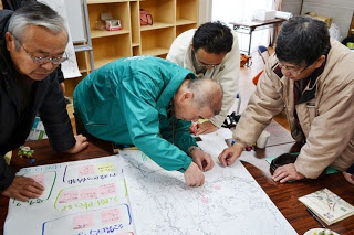 地図を囲んだ4人の男性が真剣な表情で場所を確認しながら付箋や印を貼っているマッピング作業の写真