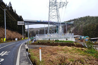 道路沿いの送電塔と周囲の木々が冬景色となっている橋の建設がほぼ完了した、完成直前の橋の写真