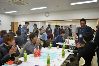 明るい室内で参加者たちがグループに分かれて談笑しながら意見交換をしている様子がにぎやかに映っている写真