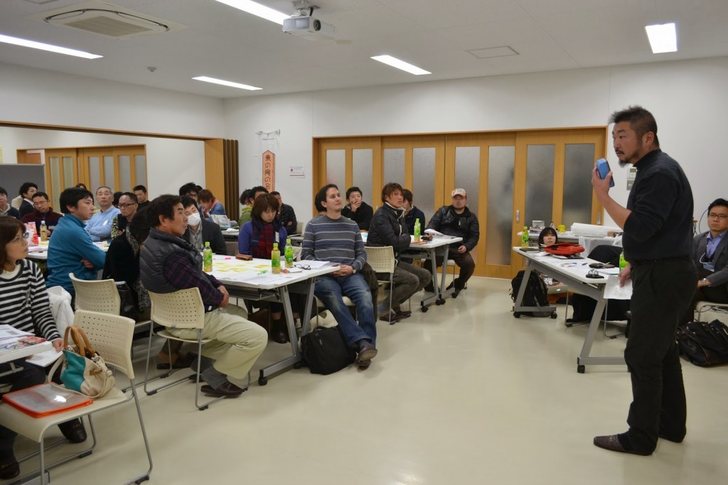 男性講師がイレーザーを左手に持ちながら話しており、多くの参加者が座って前方を見ている写真