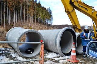 大きな丸い土管が3ケ並べられ、重機で運ぼうとしている建設現場の写真