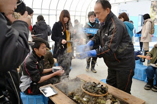 大学生たちがご主人の賢一さんから牡蠣を皿に入れてもらっている写真